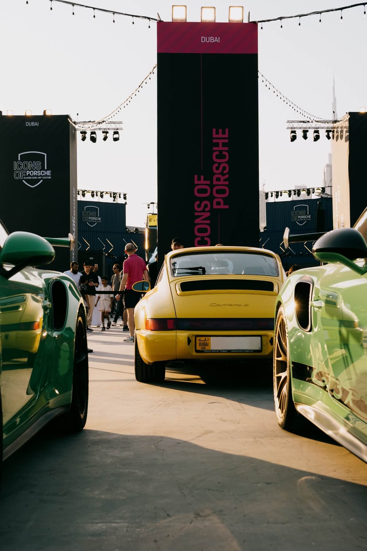 Classic yellow Porsche in between 2 other cars in Dubai IOP festival