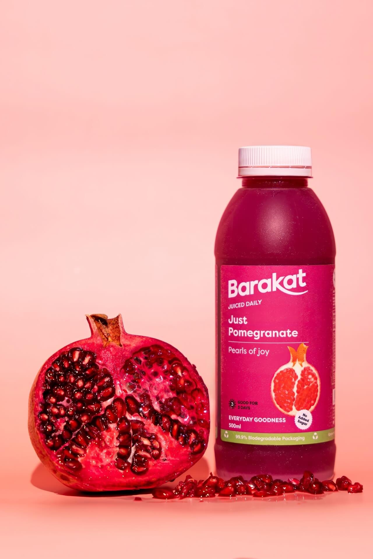 Barakat Pomegranate bottle next to a pomegranate on a pink background