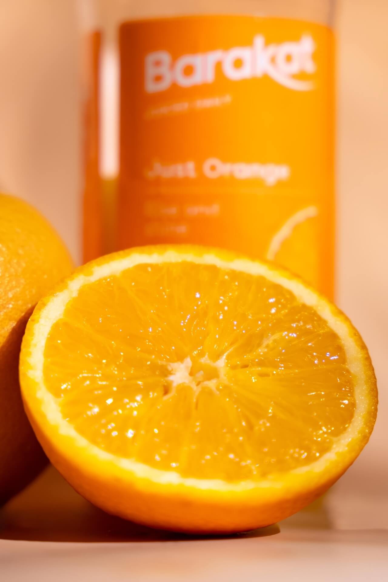 Close-up of an orange with Barakat orange juice bottle in the back