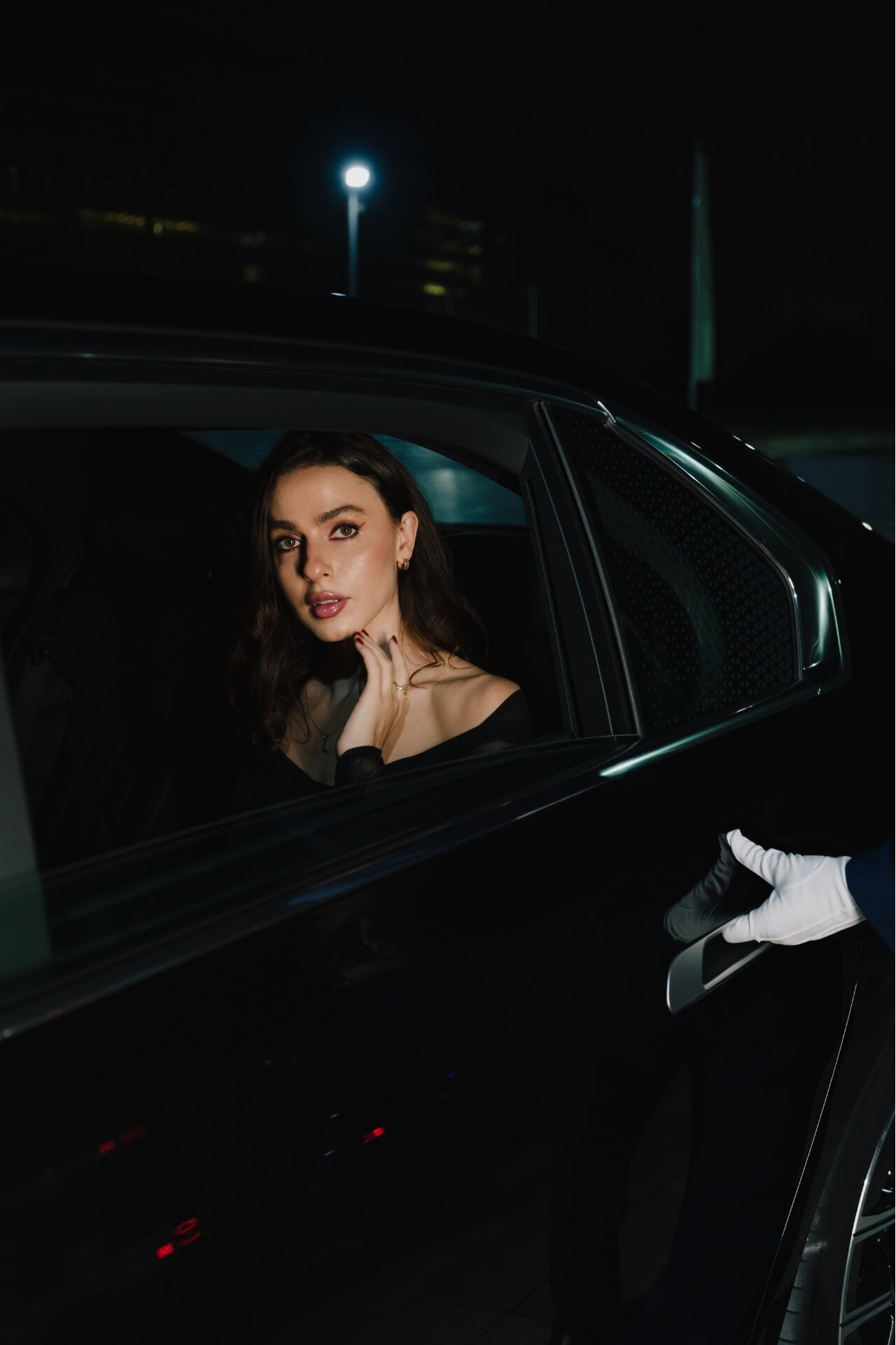 Beautiful elegant lady in the back of the car with window open and hand of valet on the handler with white gloves