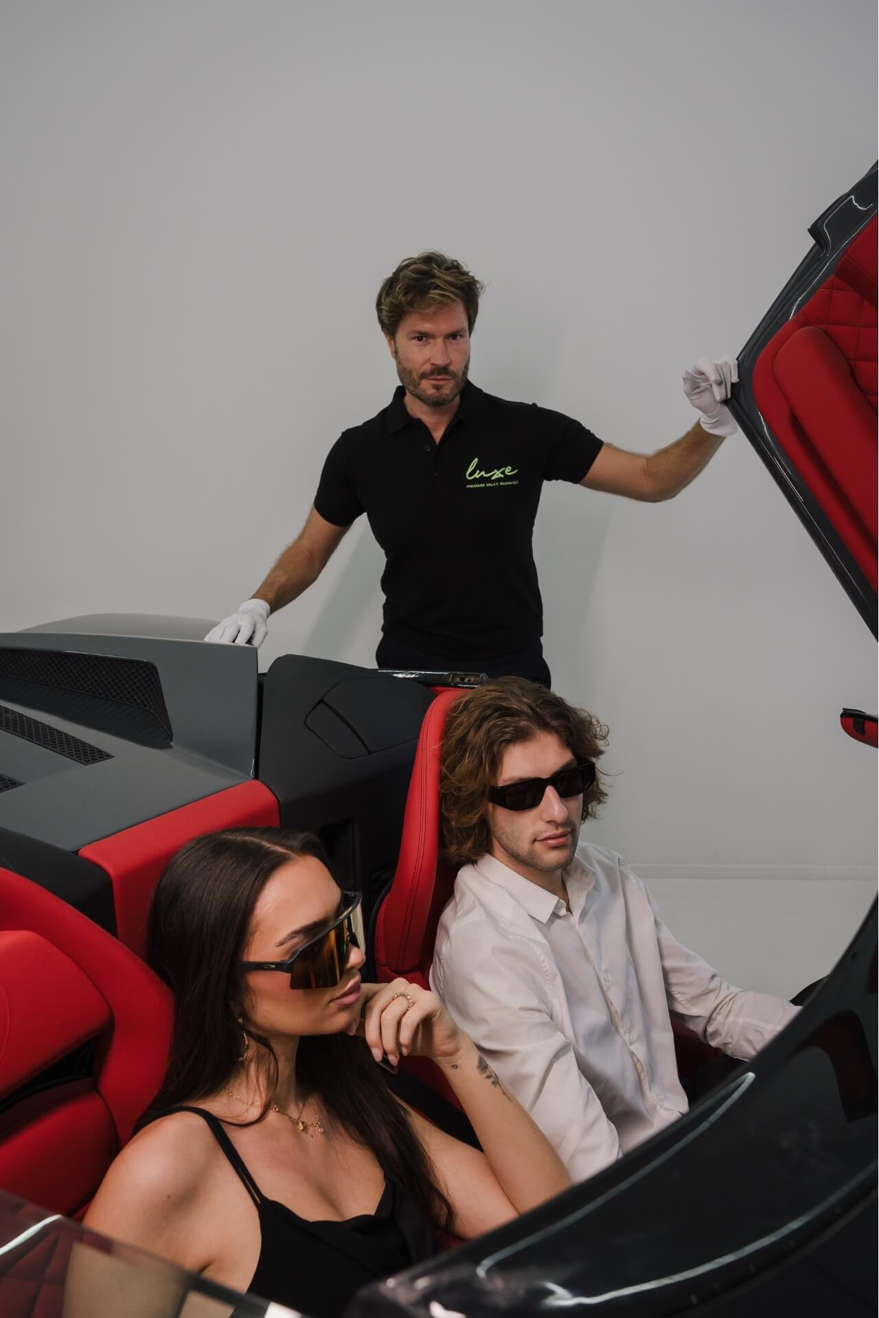 Couple in a red interior Lamborghini Murcielago with door open and valet holding it up