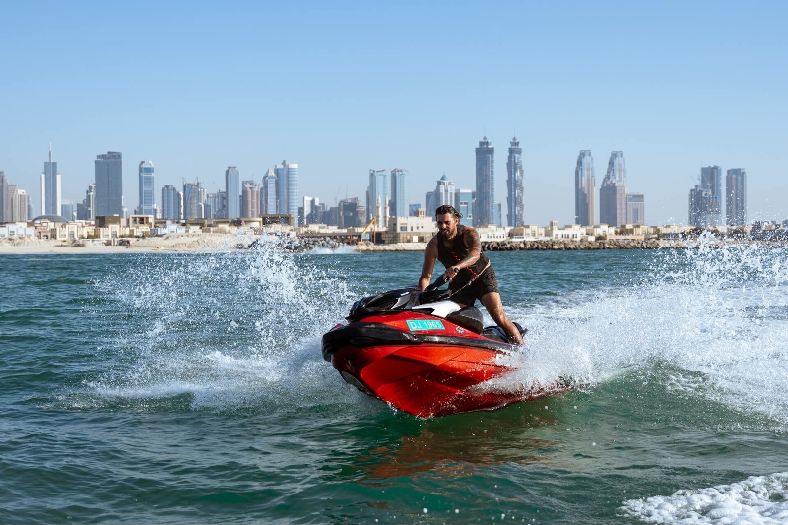 Man going fast on a red jetski splashing water close to Dubai seashore